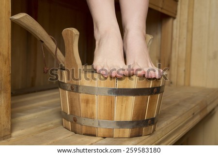 Beautiful female feet in sauna, bath accessories. Wooden bucket and sticks