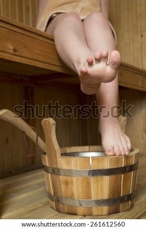 Beautiful female legs in sauna, bath accessories. Wooden bucket