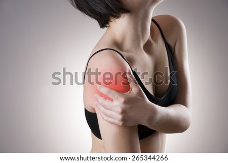 Hands on a woman\'s shoulderon gray background. Pain in the muscles. Red dot