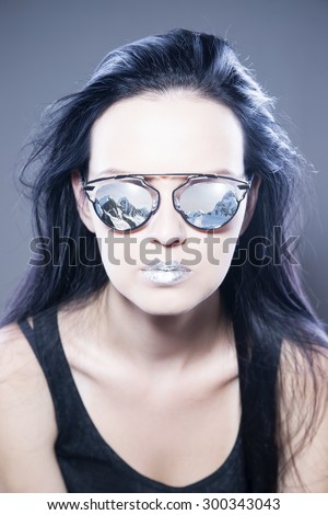 Beautiful woman fashion model portrait in sunglasses with reflections of mountains and metallic silver lips. Creative hairstyle and make up. Beauty girl on a gray background