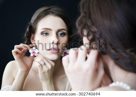 Studio portrait of a young beautiful bride looking in the mirror in a white dress. Professional make-up and hairstyle. Black background