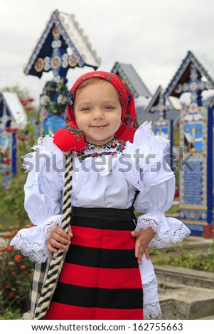 Little girl wearing romanian traditional clothing and traditional cemetery of Sapanta on a background