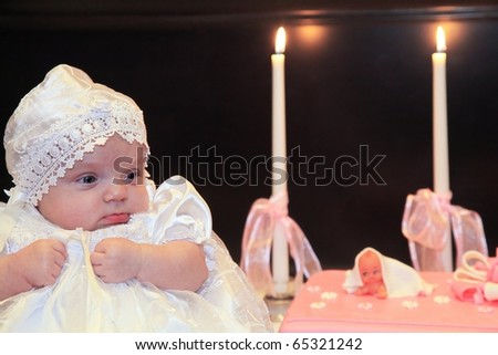Baby girl wearing a white suit and pink baptism cake on the background