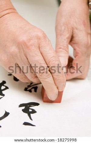 a person at a desk using a agalmatolite stamp or  seal on his Chinese calligraphy work