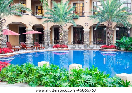 Open air swimming pool with  chaise longue under umbrella for tropical resort and plants around