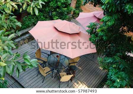 Summer Patio with tables and wooden chairs under umbrella in garden