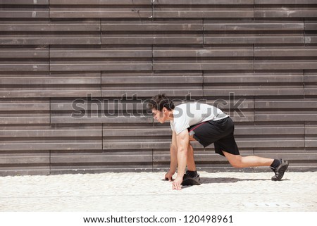 Men athlete start running next to some city wall