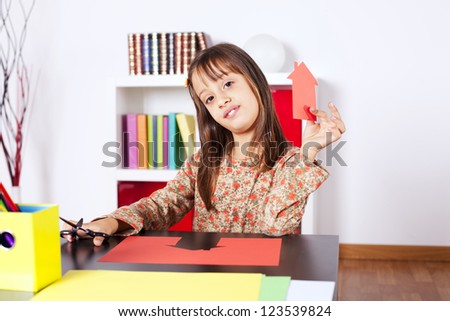 Litle girl cutting a house on a red paper