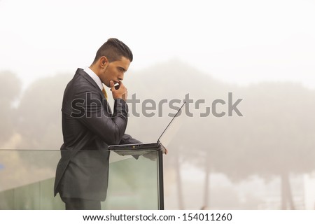 Confident young businessman working with his laptop at the office balcony