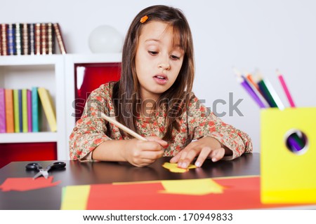Little girl cutting a house on a red paper