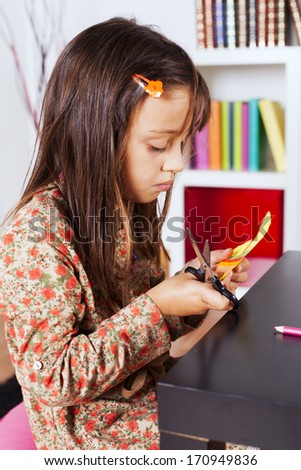 Little girl cutting a house on a red paper