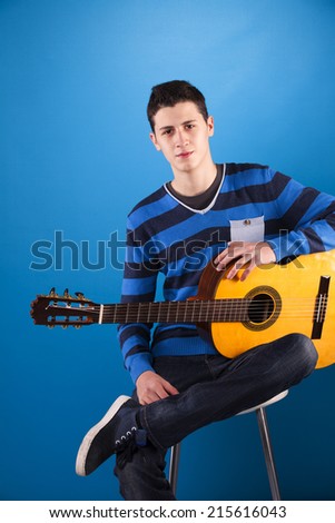 Teenager holding a classic guitar with blue background