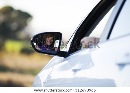 Beautiful woman face reflected on the side mirror of her new car