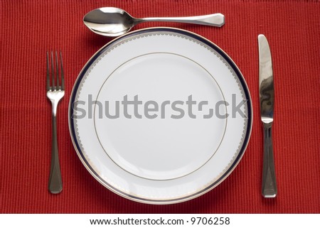 fork, knife and spoon in a porcelain plate over red (copy space in the plate)