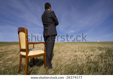 businessman standing next to a chair in outdoor looking to the field