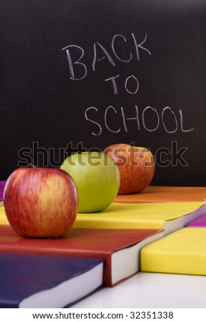 apples over a stack of books next to a chalkboard  (selective focus)