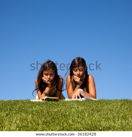 two young sisters at the park reading a book