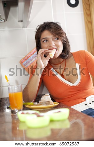 beautiful woman eating her breakfast and drinking her orange juice looking natural at her kitchen (selective focus with shallow DOF)