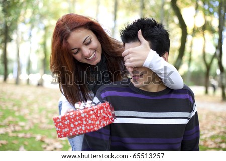 woman covering the eyes to his boyfriend with giving him a present (selective focus with shallow DOF)
