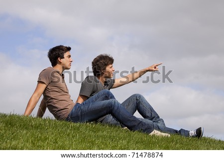 Two young men sited on the grass looking and pointing away