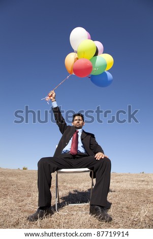 Businessman sitting in a chair at a field holding colorful balloons