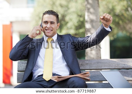 happy businessman in the park at the telephone, receiving good news