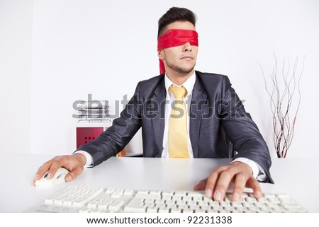 Businessman at his office with scarf covering his eyes while working with his computer