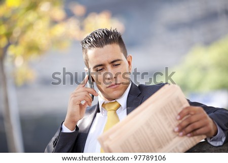 Businessman calling at the cellular and reading his newspaper