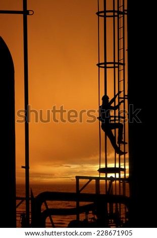 Worker climbing up gas refinery ladder