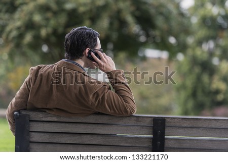 Man Sitting On Park Bench Talking On Mobile Phone