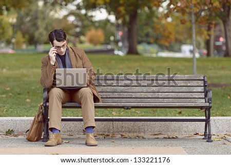 Young Man Sitting On Park Bench, Looking Bored With His Work