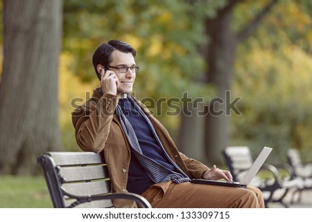 Positive Young Man Multitasking On A Park Bench