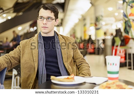 Apathetic Young Man Eating Pizza At The Food Court In A Mall