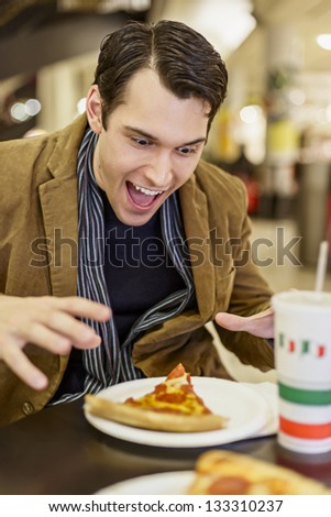 Young Man Eating Pizza At The Food Court In A Mall
