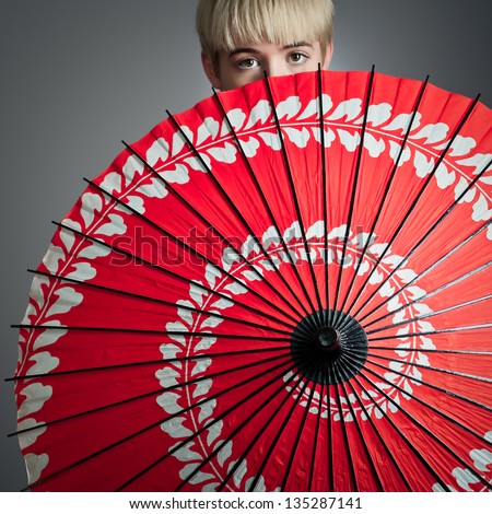 A short haired girl peeking over her red parasol.