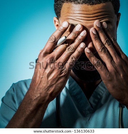 Studio shot of a young African American doctor suffering fatigue and rubbing his eyes.