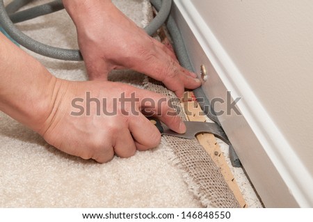 A man pulls back carpet in order to install insulation under the molding.
