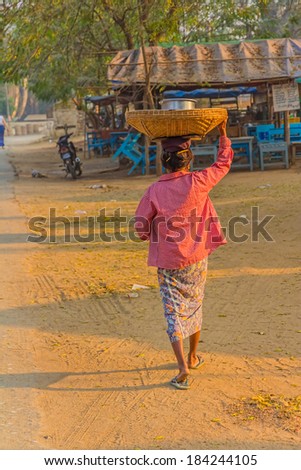 MINGUN, MYANMAR - FEBRUARY 26, 2013: A woman leaves the market with a basket on her head.