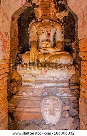 INDEIN, MYANMAR - FEBRUARY 28, 2013: Ruined statue at the entrance of the ancient Stupas overgrown with plants.