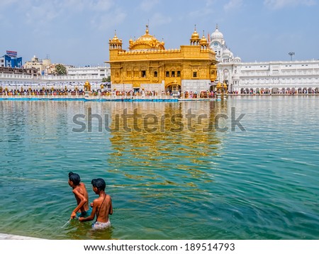 AMRITSAR, INDIA - MARCH 30, 2010: Two Sikh boys walking in a pool in front of the Golden Temple while Tourists and pilgrims entering  and walk towards The Harmandir Sahib (Golden Temple).