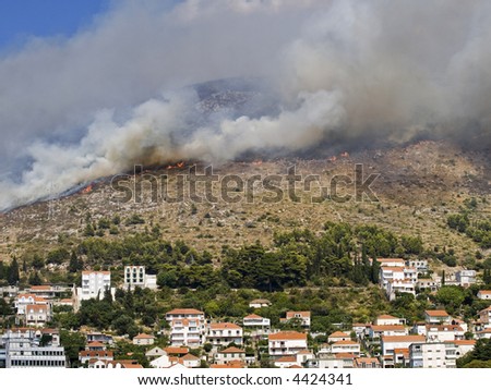 Fire line with smoke. Mediterranean hill with typical grass and small trees is burning near city.