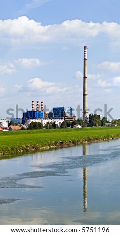 Heating and power plant near river against blue sky and green plants