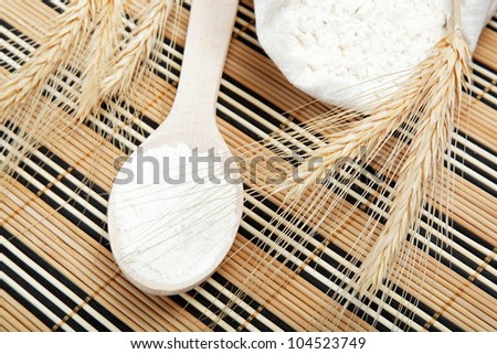 Flour and wheat grain with wooden spoon on a wooden table.