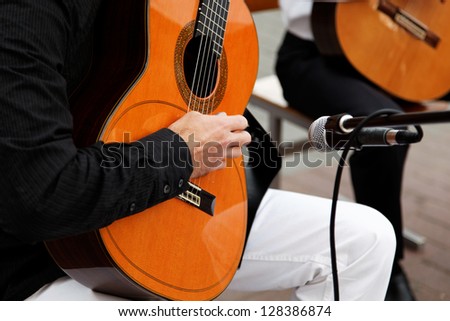 Acoustic guitar in the hands of a street musician with a microphone.