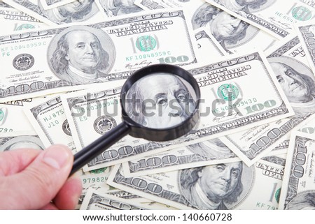 Hand with magnifying glass on a background of dollar bills. The note under a magnifying glass.