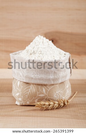 Flour in a canvas bag and ear of wheat on the wooden board.