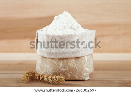 Flour in a canvas bag and ear of wheat on the wooden board.