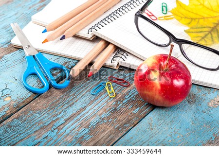 Notepad, pencils, scissors, paper clips and glasses. Office or school supplies on wooden planks painted in blue.