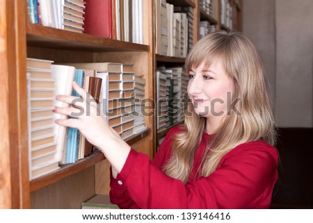 young woman in the library standing near the bookshelves and takes the book