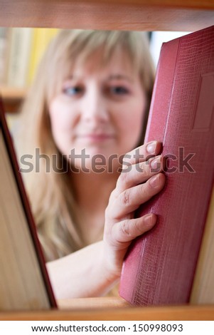 serious girl takes a book from the shelf in the library